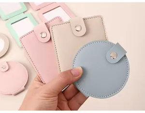 Close-up of colorful round and square PU leather portable makeup mirrors held in a hand.