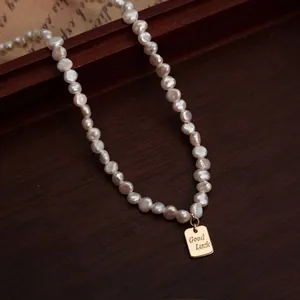 Detalle de un collar de perlas barrocas con un colgante rectangular dorado Good Luck.