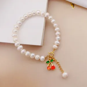 Dettaglio del bracciale di perle bianche con ciondolo a ciliegia rossa e chiusura oro.