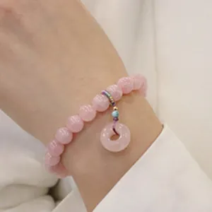 Dettaglio macro di un braccialetto di perle di agata rosa con ciondolo ping'an kou