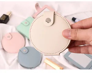 Close-up of portable PU leather mini makeup mirror in hand, soft pastel colors.