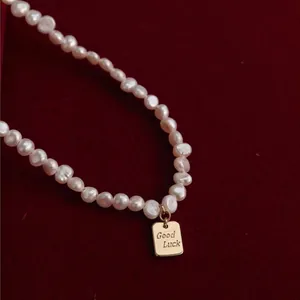 Primer plano de un collar de perlas barrocas con colgante dorado Good Luck.