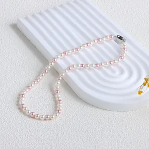 Élégant collier de perles de nacre colorées sur un présentoir blanc minimaliste.