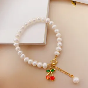 Dettaglio di un elegante bracciale di perline bianche con un grazioso ciondolo a ciliegia