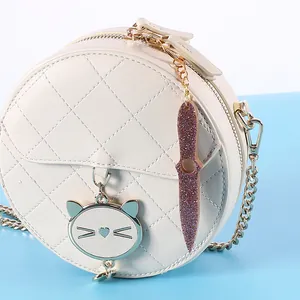 Detail of a white round quilted crossbody bag featuring a glittery purple kunai charm