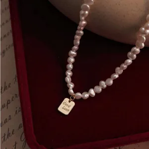Primer plano de un collar vintage de perlas barrocas con colgante dorado Good Luck detalle