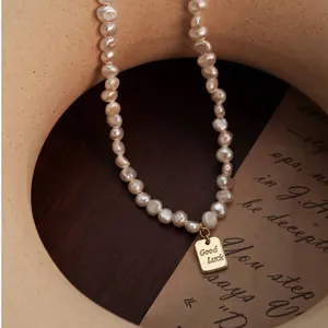 Primer plano de un collar vintage de perlas barrocas con colgante dorado grabado 'Good Luck'.