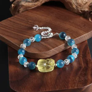 Makroaufnahme eines Armbands aus blauem Achat mit gelbem Pixiu-Anhänger auf Holz.