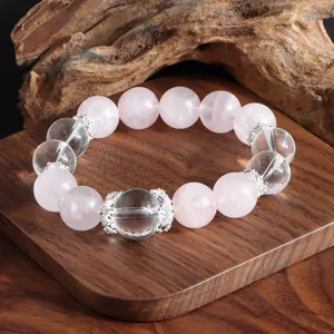 Détail du bracelet en quartz rose et cristal de roche sur un support en bois rustique.