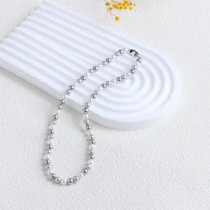 Gros plan d'un collier de perles de coquillage colorées sur un socle blanc texturé