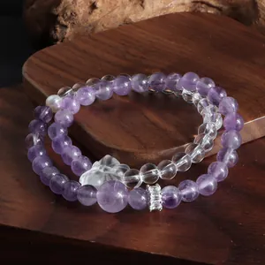 Gros plan d'un bracelet en améthyste et cristal clair avec perle et pendentif floral.