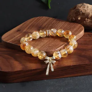Detailansicht eines natürlichen Citrin-Kristallarmbands mit glitzerndem goldenem Schleifenanhänger.