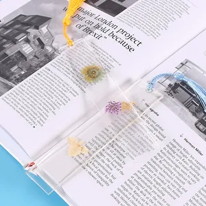 Nahaufnahme transparenter Lesezeichen mit getrockneten Blumen und bunten Quasten.