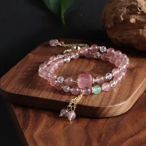 Detail view of a double-strand strawberry quartz and crystal beaded bracelet with tassels.