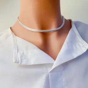 Gros plan d'un collier chaîne serpent plate argentée sur un col de chemise blanc