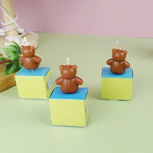 Tres velas de cumpleaños con forma de oso pardo sobre pequeñas cajas de regalo.