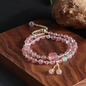 Detailed view of a strawberry quartz double-strand bracelet with elegant gold tassels on wood.