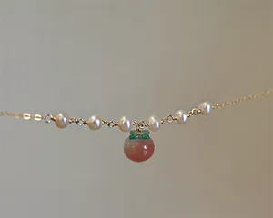 Gros plan d'un pendentif en agate rouge en forme de pêche avec perles sur chaîne en or