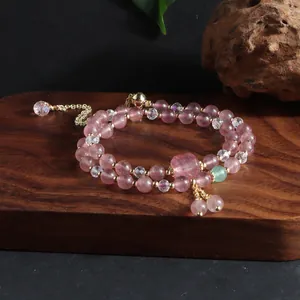 Detailed view of natural strawberry crystal double-strand bracelet with gold tassel details