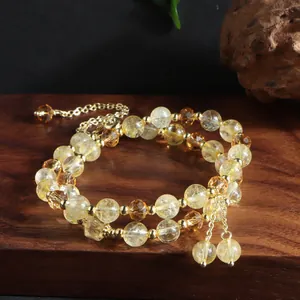 Detailed view of dual-strand natural citrine bracelet with golden tassel on wooden base