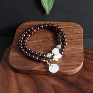 Nahaufnahme eines zweireihigen dunkelroten Perlenarmbandes mit weißem Jade-Anhänger