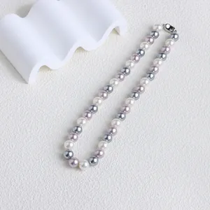 Vue de dessus d'un collier en perles de coquillage blanches, grises et lilas sur un décor