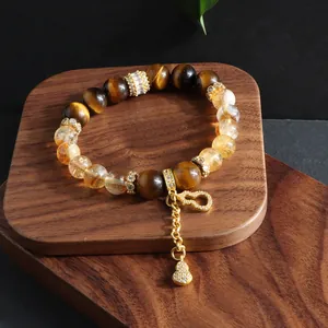 Close-up of tiger eye and citrine beaded bracelet with gold hulu charm on wood