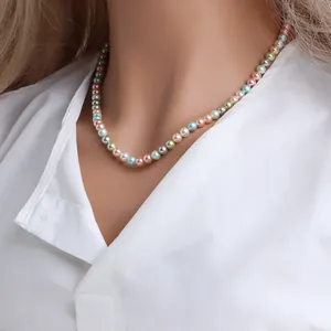 Détail d'un collier de perles rétro aux couleurs bonbon porté sur une chemise blanche.