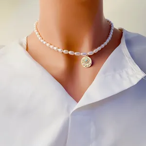 Gros plan d'un collier en perles d'eau douce avec pendentif œil doré sur blanc.