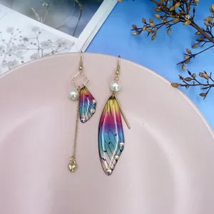 Nahaufnahme asymmetrischer bunter Zikadenflügel-Ohrringe mit goldener Herzquaste