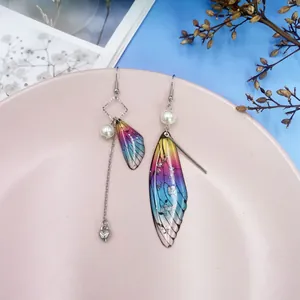 Detailansicht asymmetrischer Ohrringe mit bunten Harzschmetterlingsflügeln und Perlen.