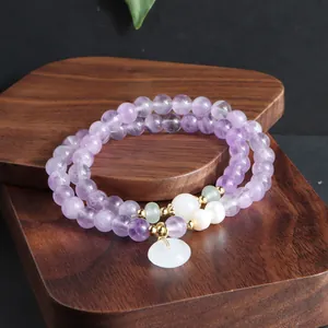 Nahaufnahme eines Amethyst-Perlenarmbandes mit Jade-Anhänger auf dunklem Holz