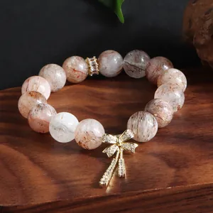 Nahaufnahme eines Naturkristall-Armbands mit goldenem Schleifenanhänger auf Holz