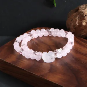 Détail macro d'un bracelet en quartz rose à double rang avec un charme en pierre de cœur.