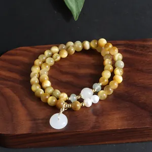 Detail eines goldenen Tigerauge-Perlenarmbands mit Weißjadenanhänger auf Holztablett