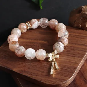 Detailansicht eines natürlichen Kristallarmbands mit goldenem Schleifenanhänger.
