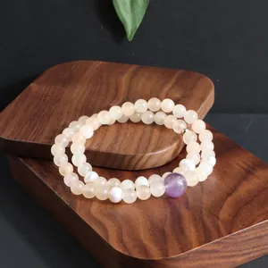 Detailopname van een dubbele edelsteen armband met paarse kunziet en witte parels op houten basis