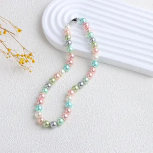 Détail d'un collier de perles de nacre aux couleurs bonbon sur un plateau ondulé blanc