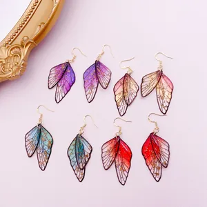 Macro view of butterfly wing earrings in four gradient colors with gold foil accents.