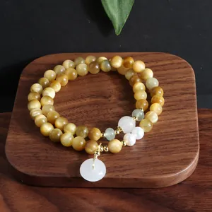 Detailansicht eines Armbands aus goldenen Tigerauge-Perlen mit Jade-Anhänger auf Holz