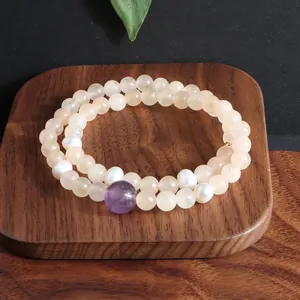 Detailopname van dubbelstrengs kristallen armband met parels en amethist op een houten dienblad.