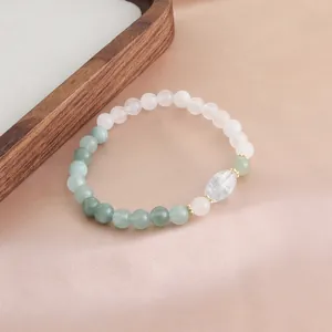 Detailansicht eines Armbands aus grünen und rosa Kristallperlen auf pfirsichfarbener Seide.