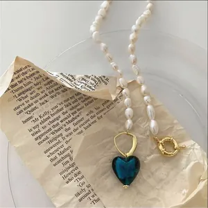 Primo piano di collana di perle barocche con pendente a cuore blu su carta vintage