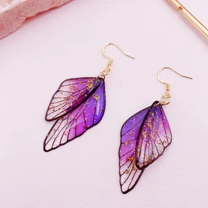 Close-up of purple gradient butterfly wing earrings with gold glitter and fishhook.