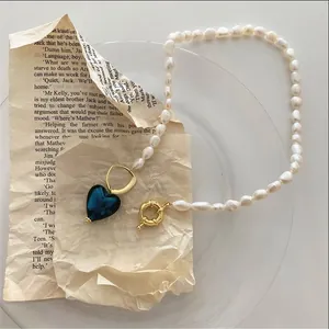 Dettaglio macro della collana di perle barocche con ciondolo a cuore blu su carta vintage