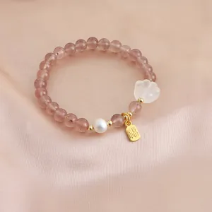 Macro view of strawberry quartz bracelet with pearl, cat paw and golden blessing charm