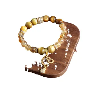 Natural yellow crystal and tiger eye beaded bracelet featuring a golden hulu charm on wooden stand.