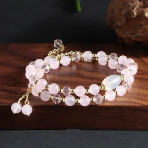 Close-up of a double-layer natural rose quartz bracelet with gold-tone tassels on wood