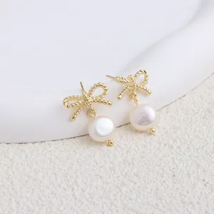 Dettaglio di eleganti orecchini a fiocco d'oro con perle d'acqua dolce naturali.