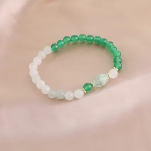Nahaufnahme des Armbands mit grünen Achaten und weißen Kristallperlen auf Satin